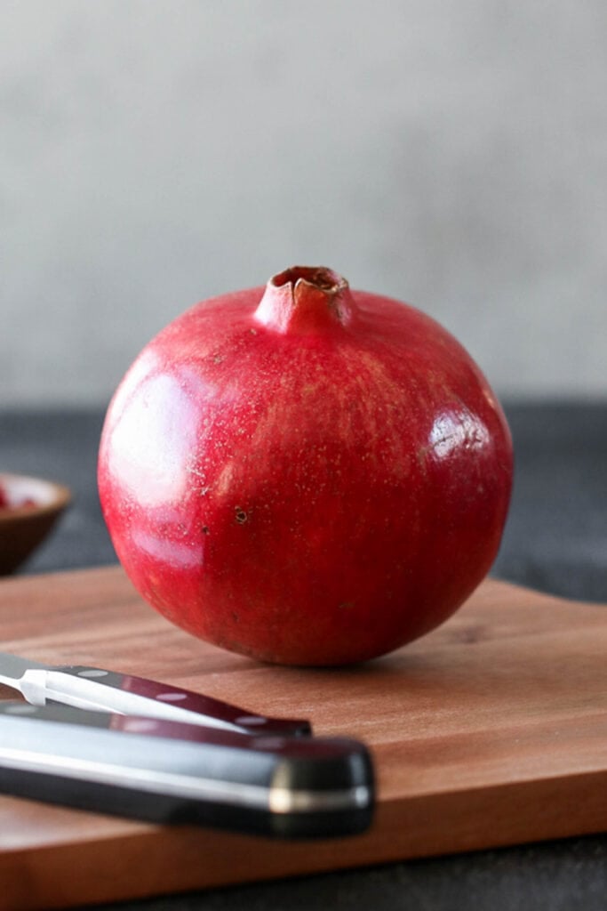 Close up view single fresh pomegranate on wooden cutting board with white background.