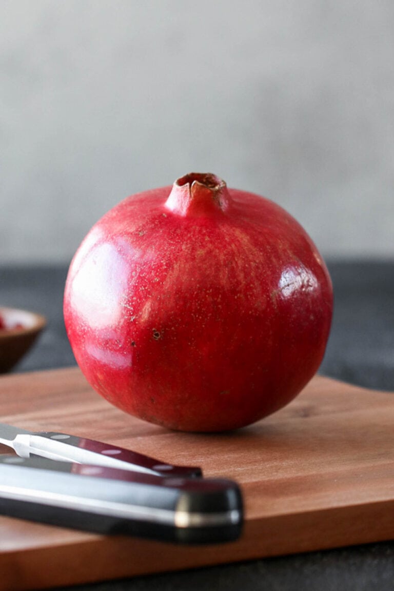 A single fresh pomegranate on a wooden cutting board.