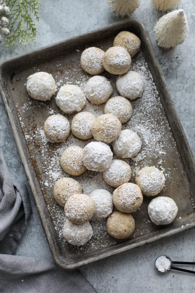 Baking sheet with several Pecan Snowball Cookies piled in, sprinkled with powdered sugar.