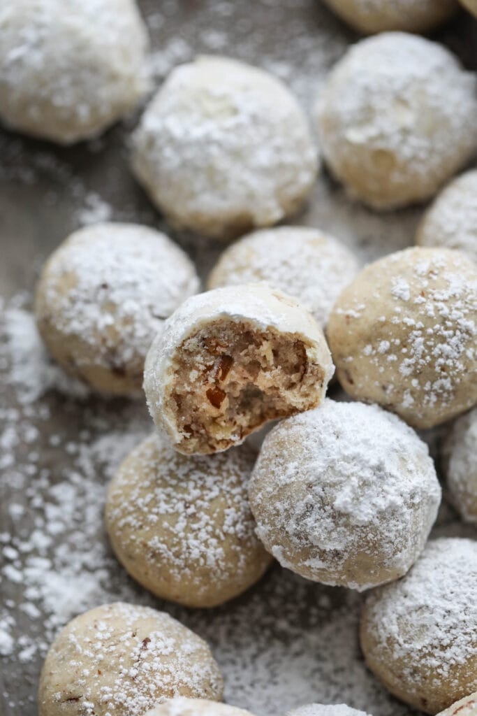 Pecan Snowball Cookies piled on baking sheet, top cookie has bite taken out to show inside texture.