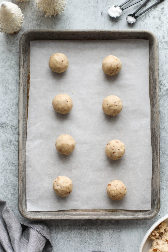 Overhead view baking sheet with lined up Pecan Snowball Cookie dough balls. 