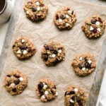 Parchment lined baking sheet with lined up trail mix breakfast cookies topped with white chocolate chips and dried cranberries.