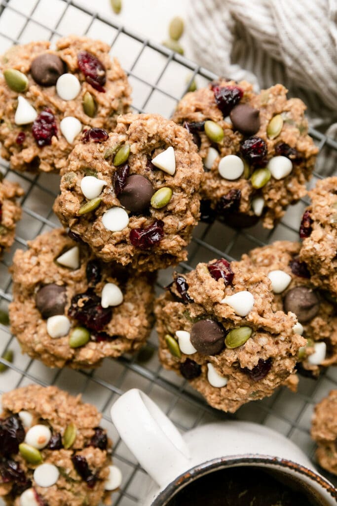 Several trail mix breakfast cookies topped with white chocolate chips, pepitas and dried cranberries on wire cooling rack.