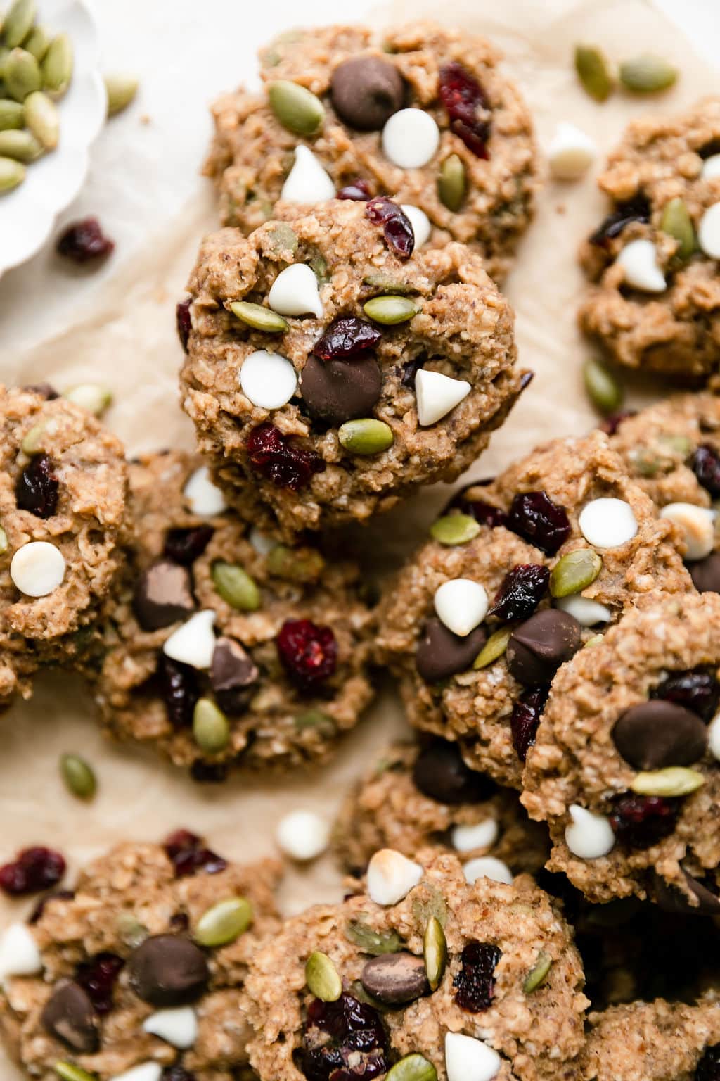 Close up view pile of trail mix breakfast cookies topped with dried cranberries, white chocolate chips, and pepitas.