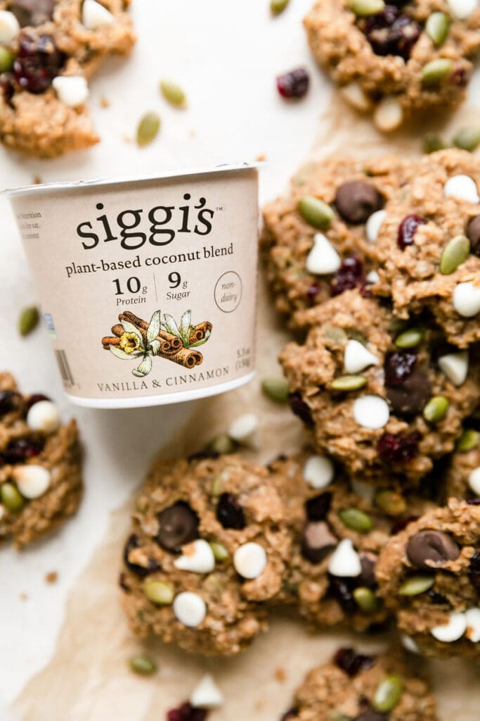 Small container Siggi's plant-based coconut blend yogurt with trail mix breakfast cookies scattered around it.