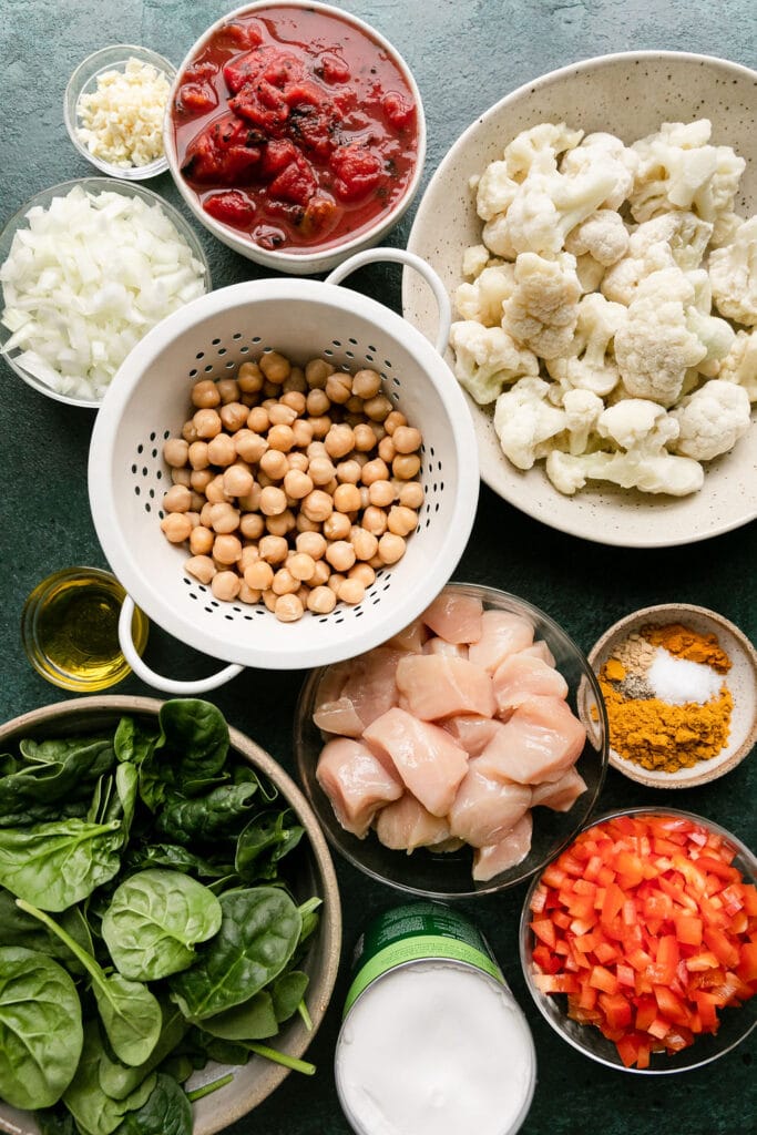 All ingredients for chicken and chickpea curry arranged in bowls and measuring cups.