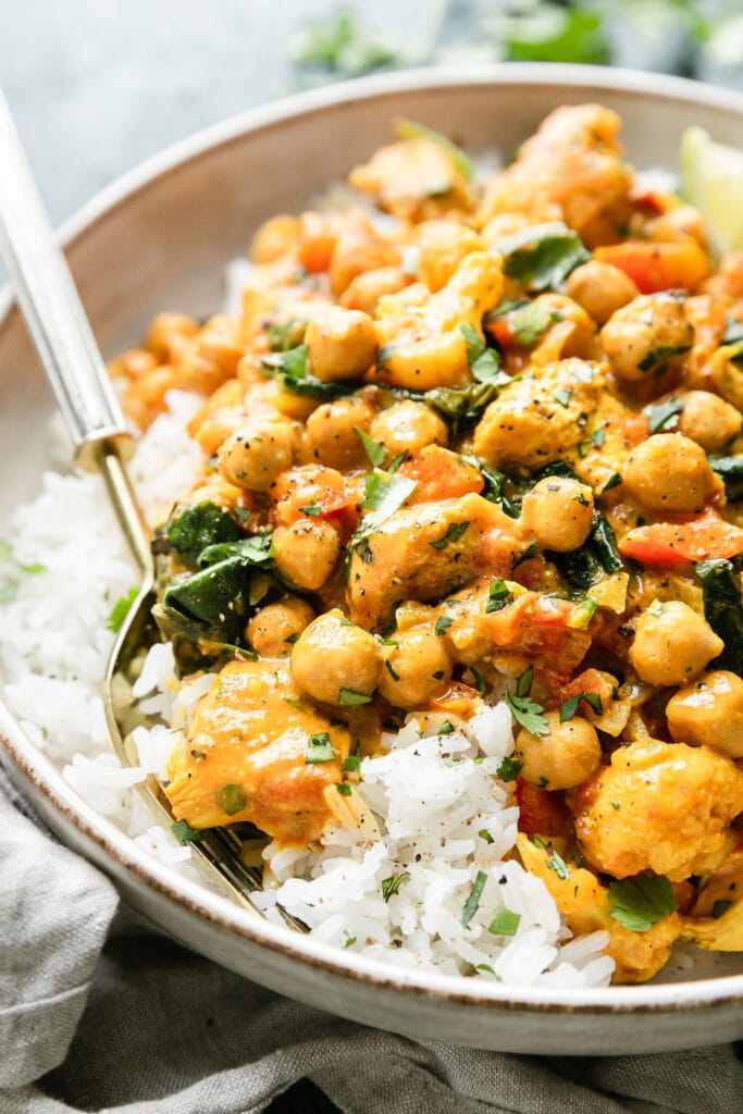 A serving of chicken curry with chickpeas and spinach served in bowl over rice.