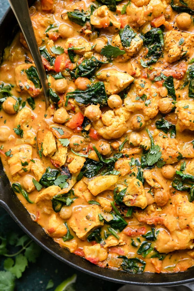 Close up overhead view chicken and chickpea curry with spinach and cauliflower in cast iron skillet.