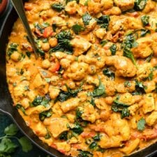 Overhead view cast iron skillet filled with chicken curry with chickpeas, cauliflower and spinach.