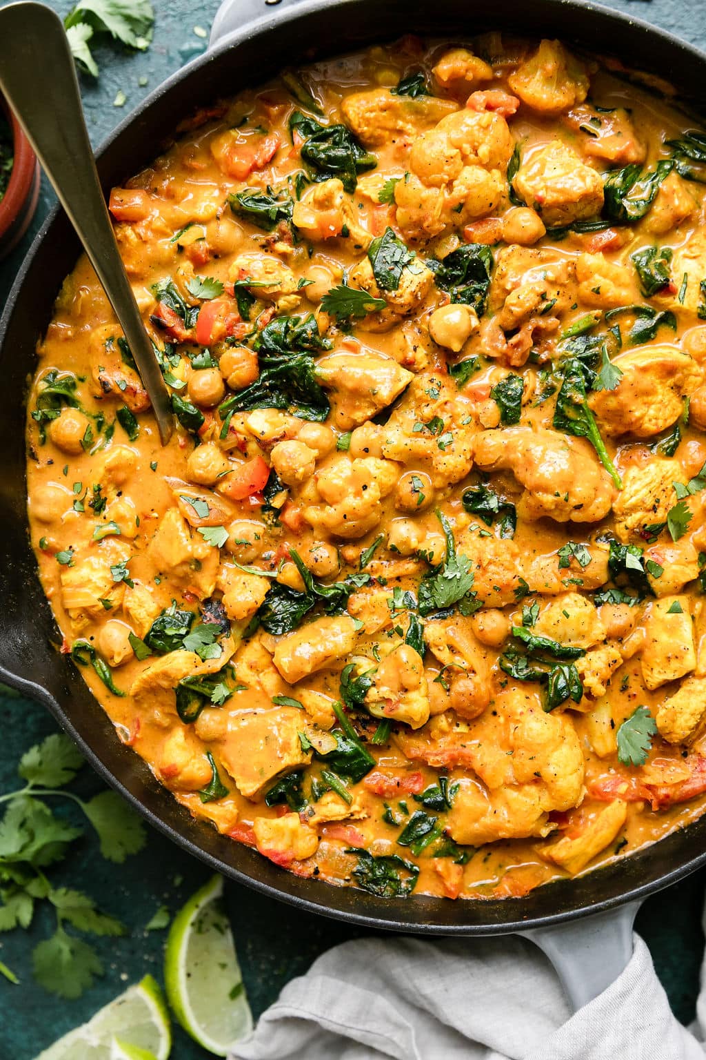 Overhead view cast iron skillet filled with chicken curry with chickpeas, cauliflower and spinach.