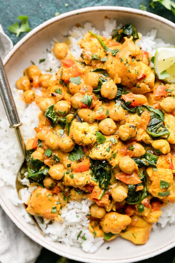 Close up view serving of chicken curry with chickpeas, cauliflower, and spinach served over rice.