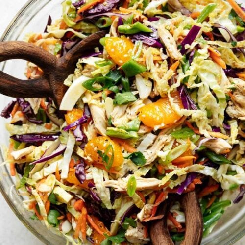 Overhead view Chinese chicken salad in clear glass mixing with wooden spoons in salad