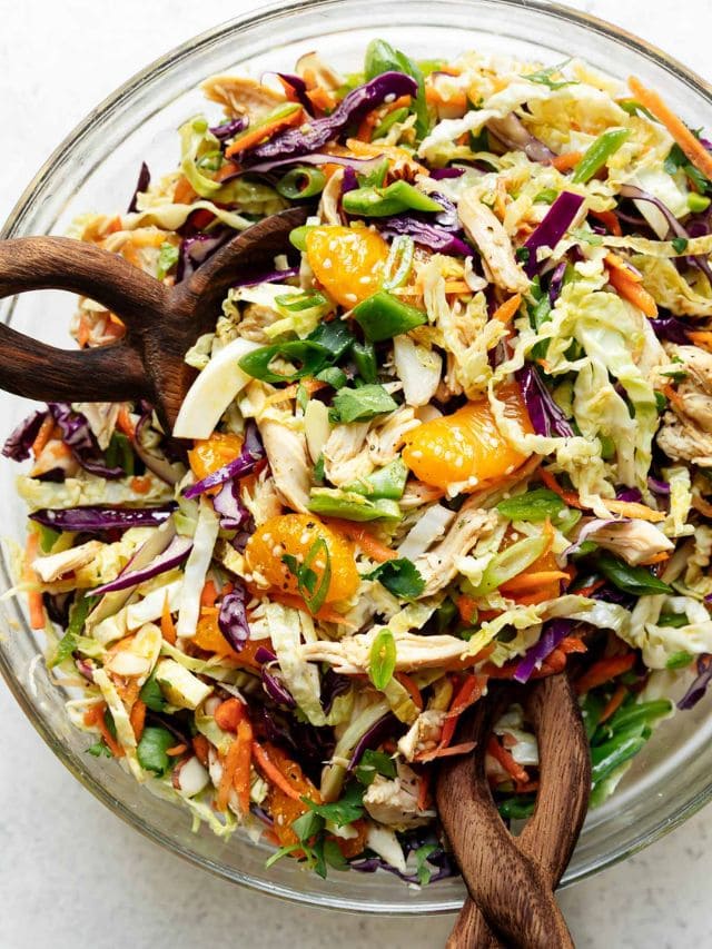 Overhead view Chinese chicken salad in clear glass mixing with wooden spoons in salad