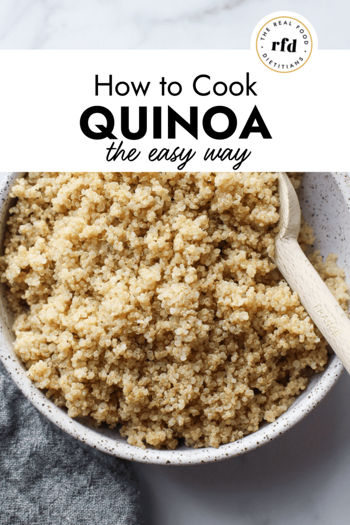 Overhead view stone bowl filled with cooked quinoa, wooden spoon in quinoa.