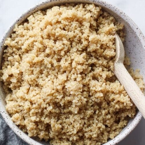 Cooked quinoa in stone bowl with wooden spoon