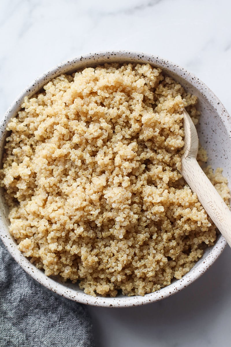 A wooden spoon in cooked quinoa in a stone bowl