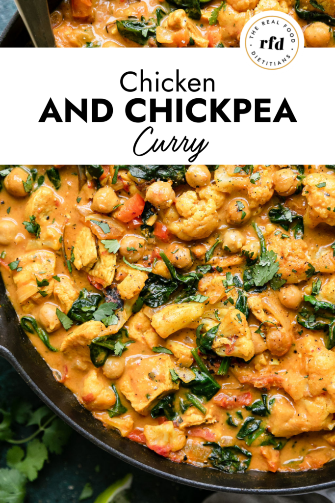 Chicken and chickpea curry in orange sauce with cauliflower and spinach in cast iron skillet with gold serving spoon.