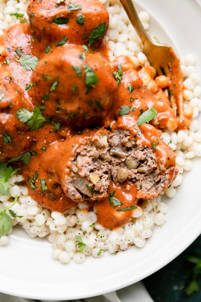 A beef and lentil meatballs cut in half to show texture, coated in red sauce served over couscous