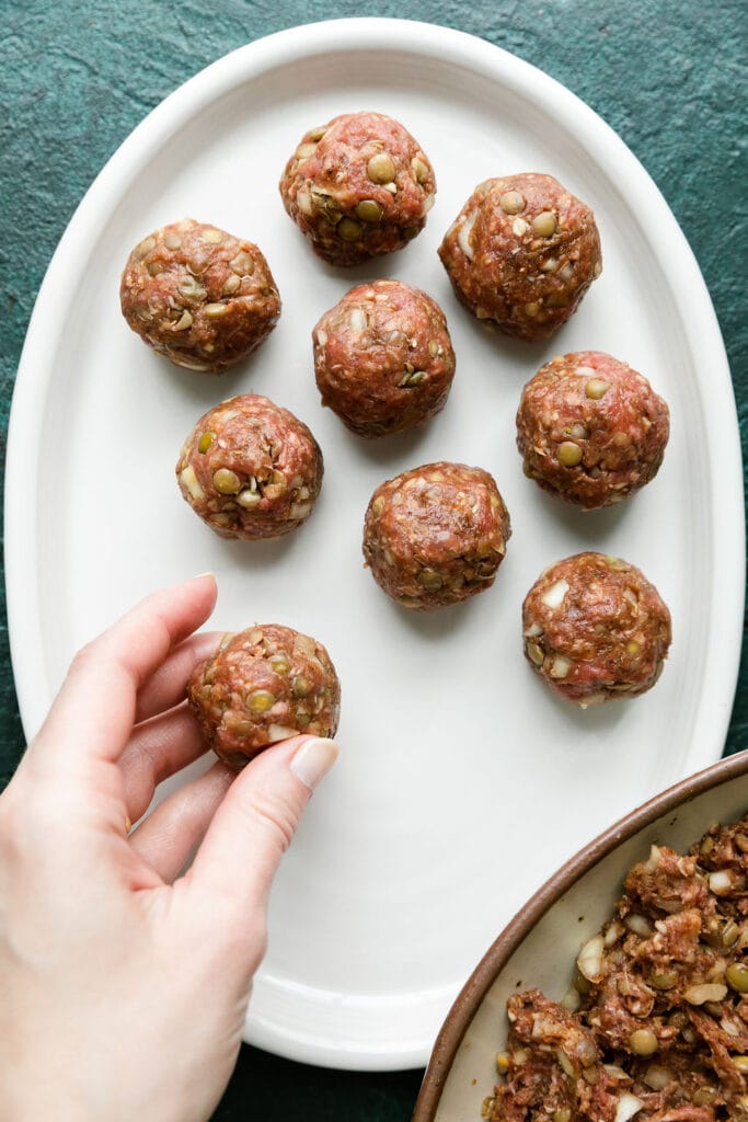 Beef and lentil meatballs being rolled out and placed on white tray.