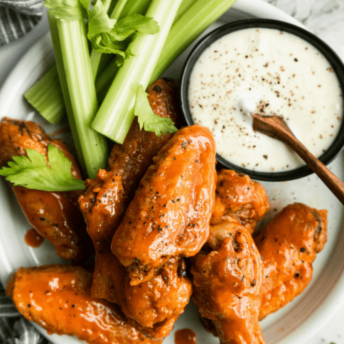 Overhead view air fried chicken wings coated in buffalo sauce on white platter with celery and ranch dressing.