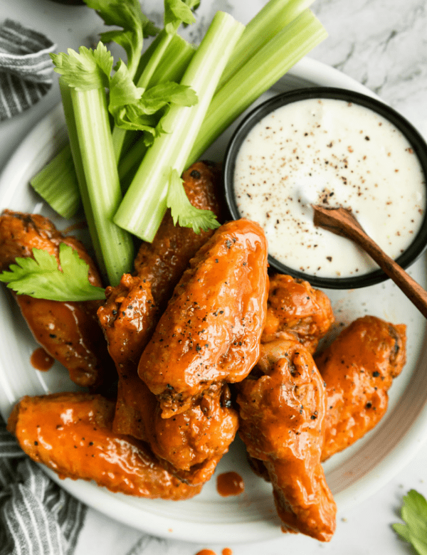 Overhead view air fried chicken wings coated in buffalo sauce on white platter with celery and ranch dressing.