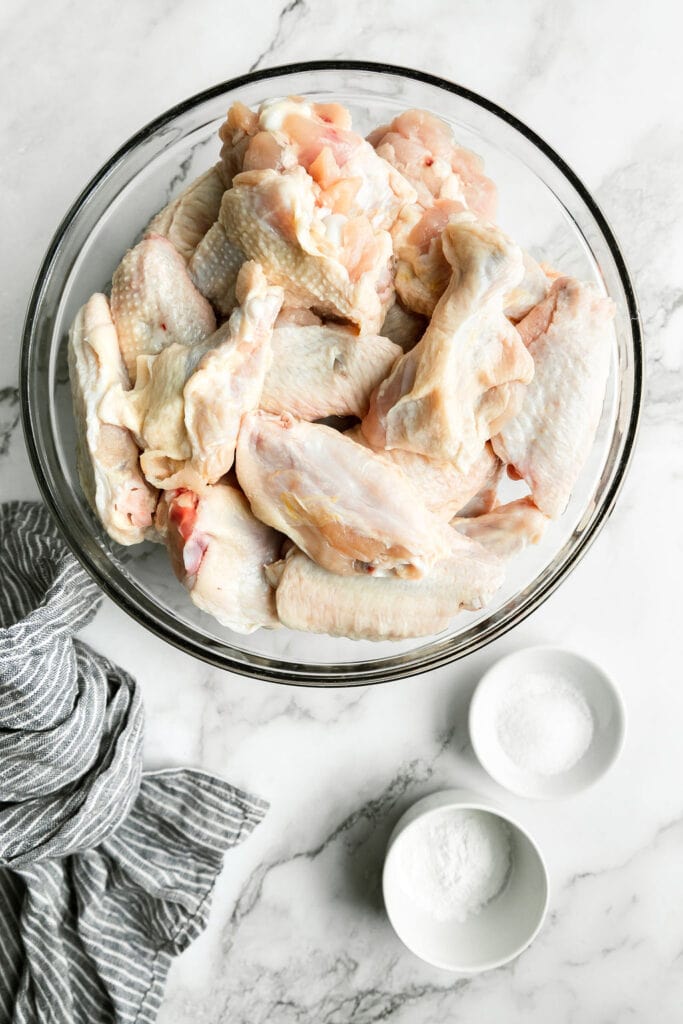 Clear glass mixing bowl filled with raw chicken wings and legs.