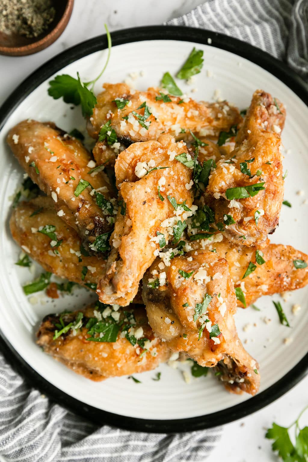 Overhead view parmesan and herb coated air fryer chicken wings on white plate.