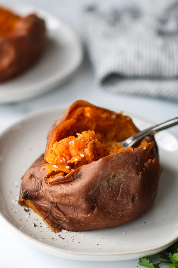 A cooked sweet potato cut open to show fluffy inside, a fork lifting up forkful