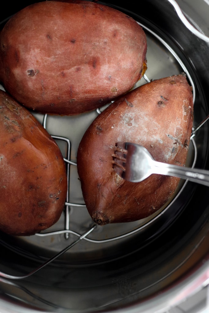 Three cooked sweet potatoes in instant pot, a fork poking into one