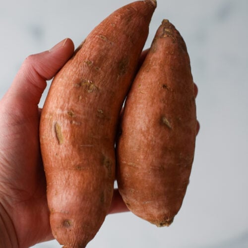 A hand holding two small sweet potatoes against marble background