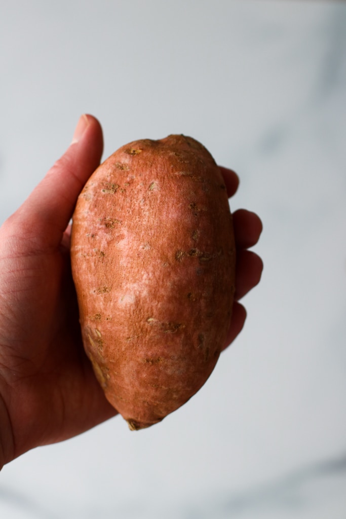 One medium sweet potato being held up against white background