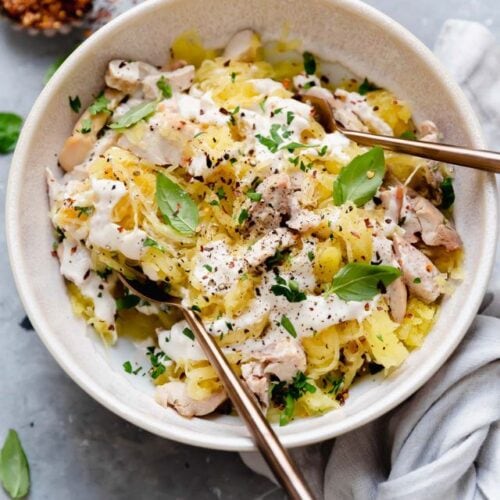 Overhead view spaghetti squash chicken alfredo in stone bowl topped with fresh basil.