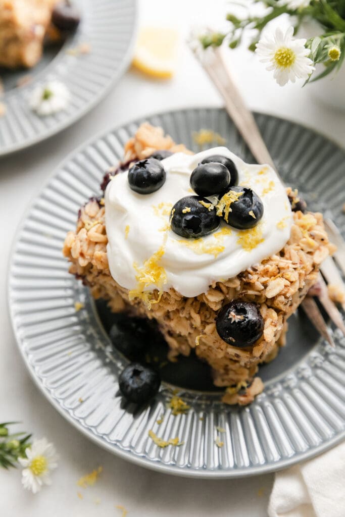 A serving of blueberry lemon baked oatmeal topped with yogurt, lemon zest and blueberries on blue plate.