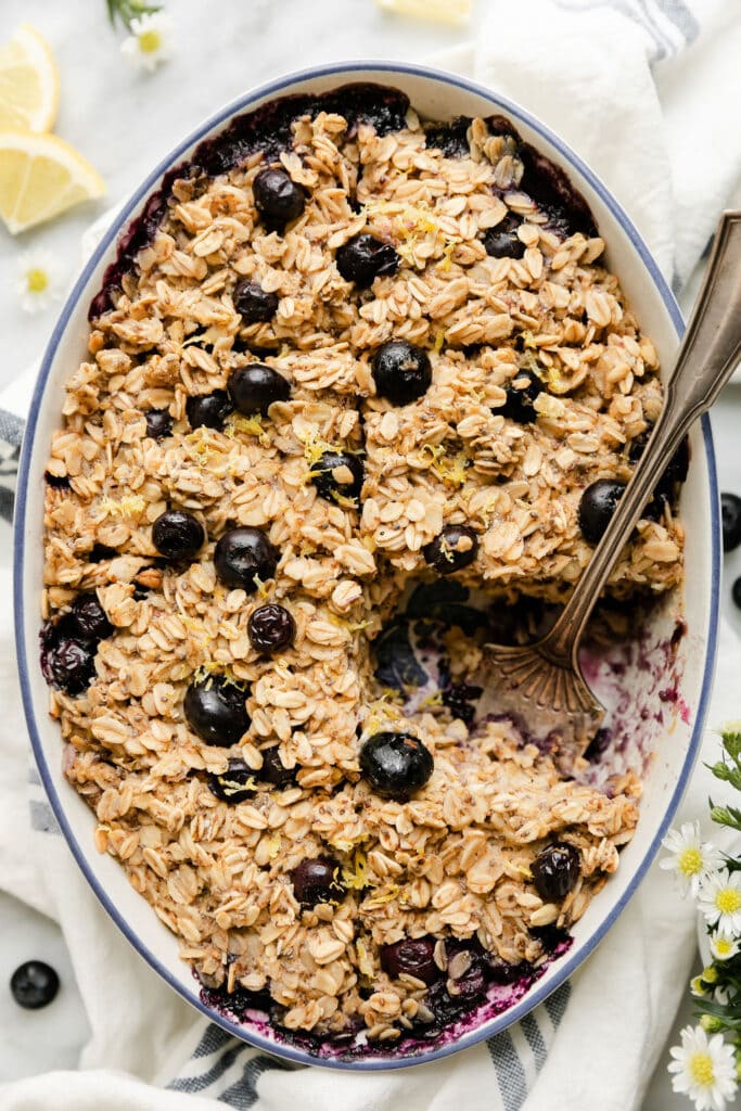 Overhead view oval baking dish filled with blueberry lemon baked oatmeal, one serving removed.