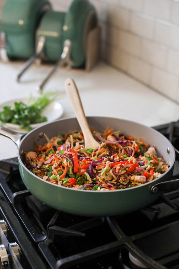 A green Caraway skillet on stovetop with Pad Thai cooking in it