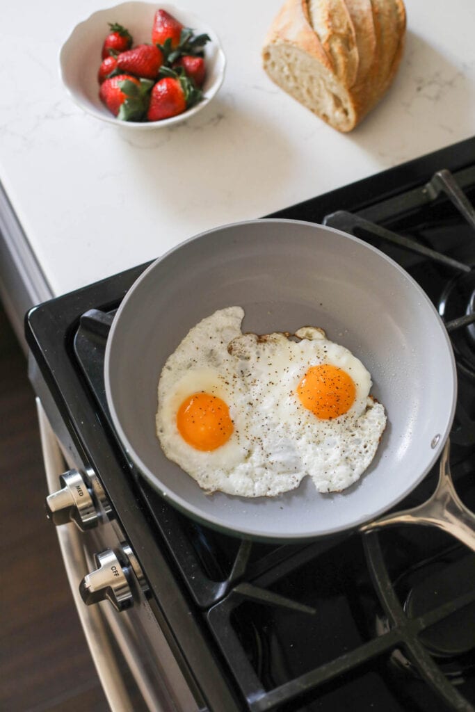 A skillet on stovetop with two eggs cooking in it