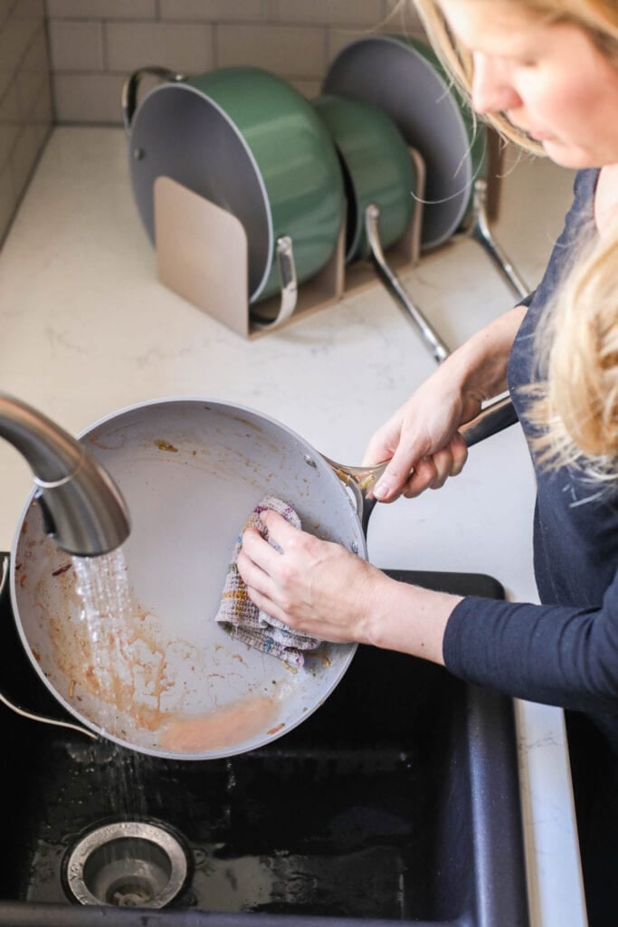 A green Caraway skillet being washed in sink