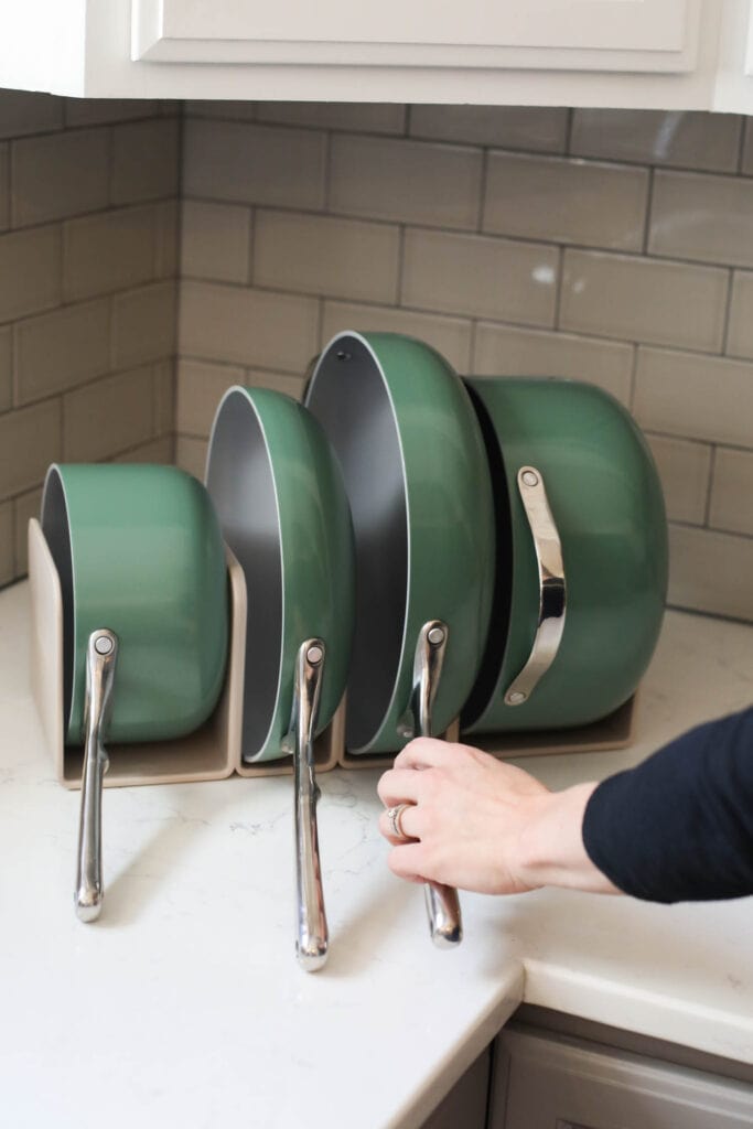 A set of green Caraway cookware on countertop, a skillet being removed from set