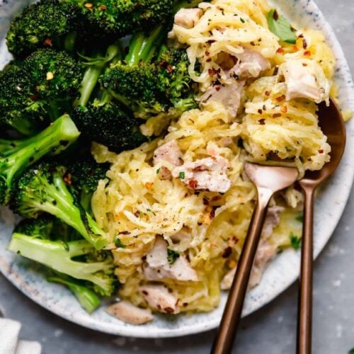 Serving of chicken alfredo with spaghetti squash on stone plate with broccoli.