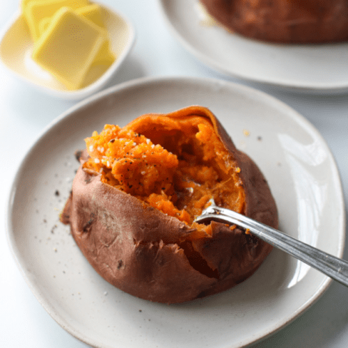 Instant Pot Sweet Potato on plate, cut open with fork in fluffy orange insides.