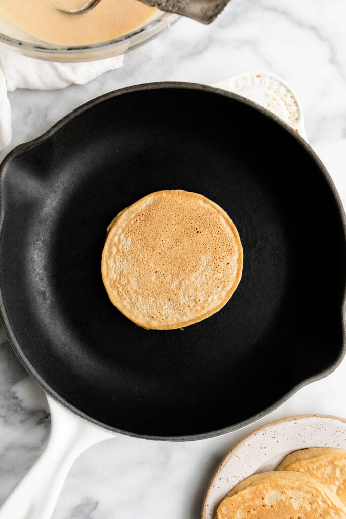 A protein pancake light golden brown in white and black skillet