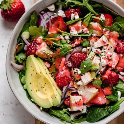 Overhead view white serving bowl filled with strawberry spinach salad with chicken and avocado.
