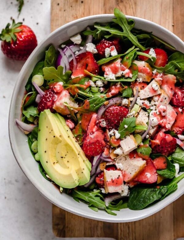 Overhead view white serving bowl filled with strawberry spinach salad with chicken and avocado.