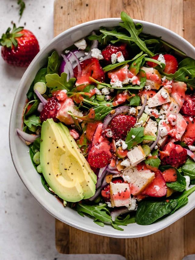 Overhead view white serving bowl filled with strawberry spinach salad with chicken and avocado.