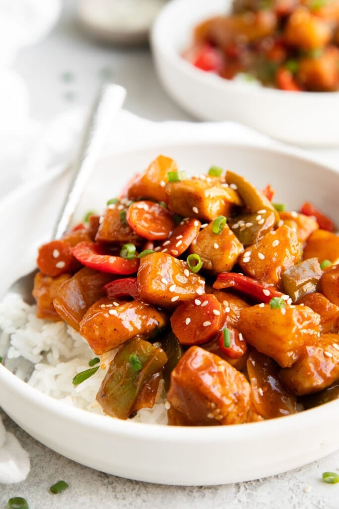 Sweet and sour chicken served over rice in white bowl