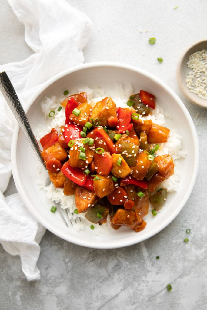 Serving of sweet and sour chicken over rice in white bowl