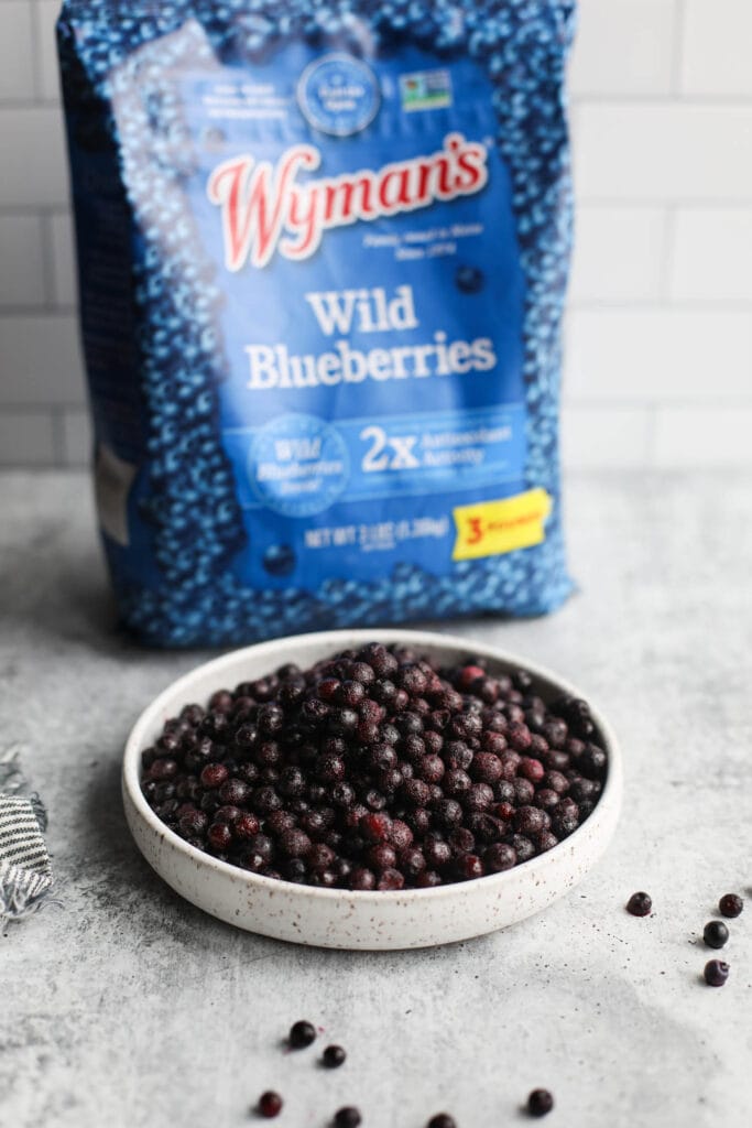 Stone bowl filled with wild blueberries, blue bag of Wyman's wild blueberries in background