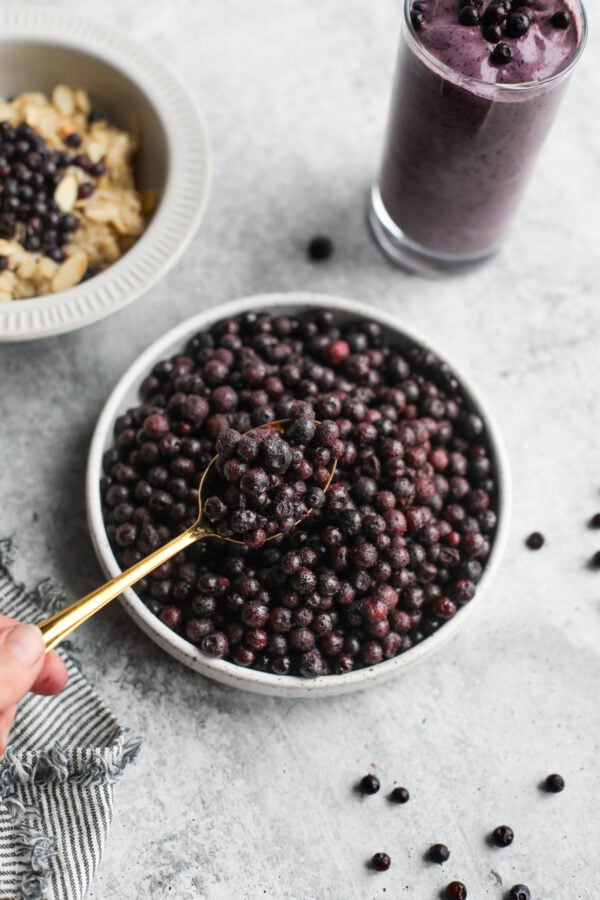 Gold spoon with spoonful of wild blueberries over stone bowl filled with berries