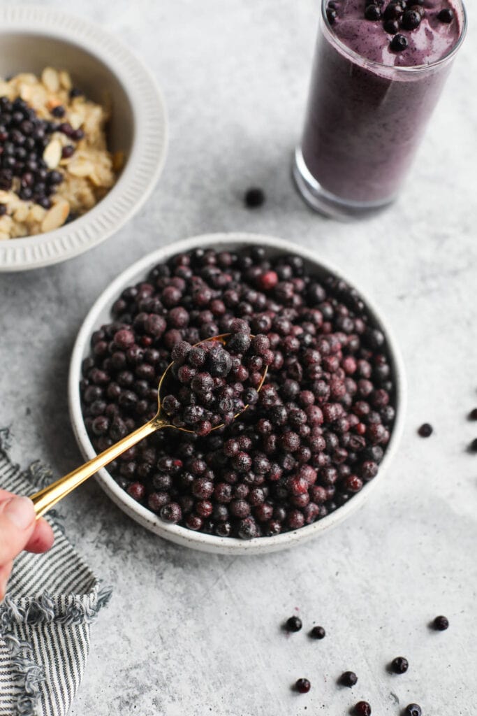A gold spoon scooping up spoonful of wild blueberries from stone bowl