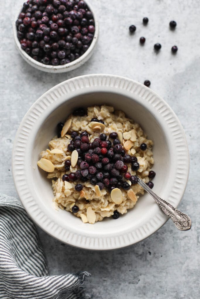 Overhead view white bowl filled with oatmeal topped with almonds and wild blueberries